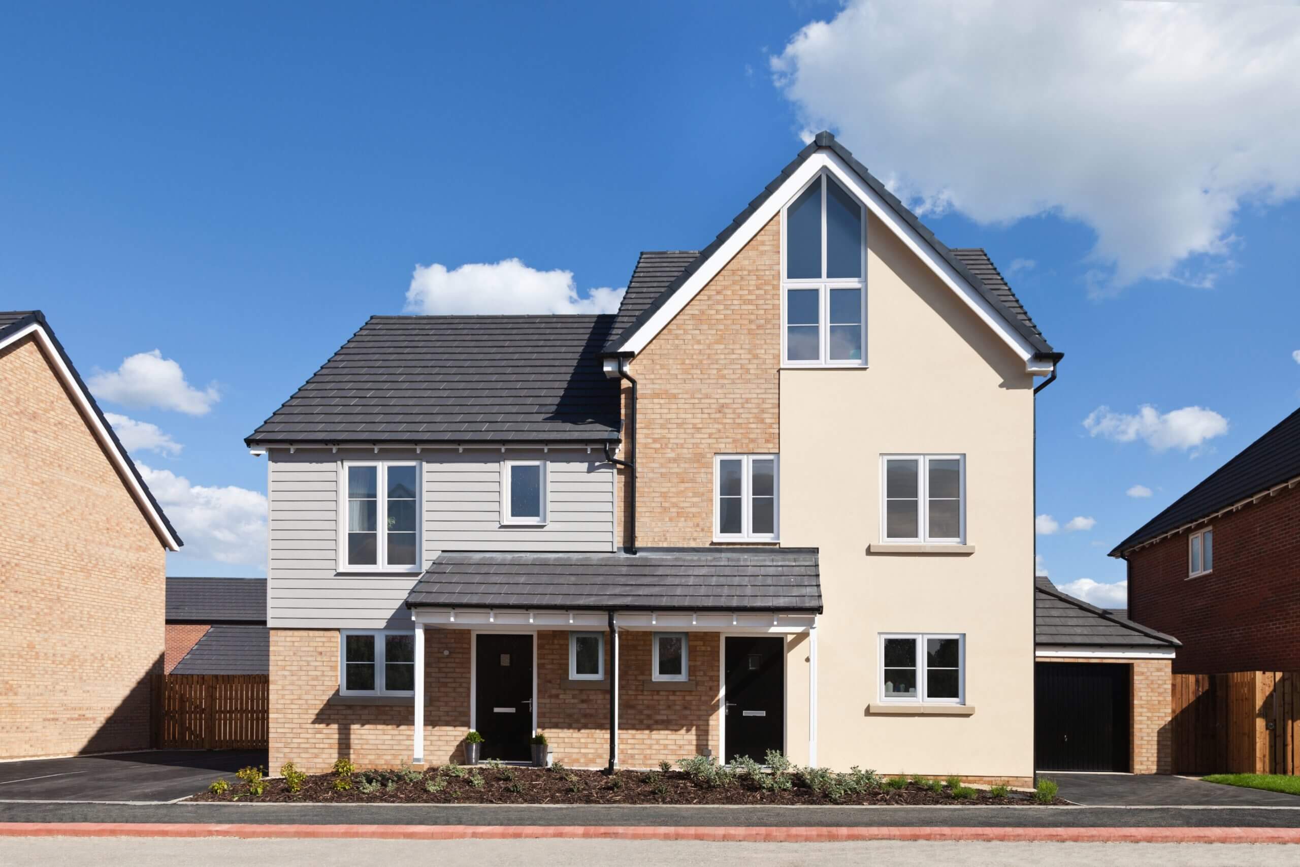 A contemporary detached house with a two-tone brick and siding façade, featuring white uPVC Casement windows under a grey shingle roof, with a landscaped front garden and clear blue skies above.