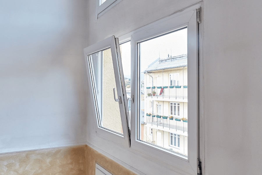 The image shows an open Upvc tilt-and-turn window in a white room, overlooking a building with balconies