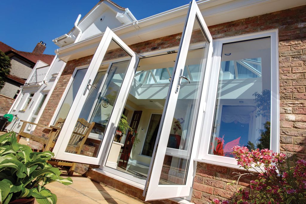 Open white French doors of a house with a view into the sunny interior.
