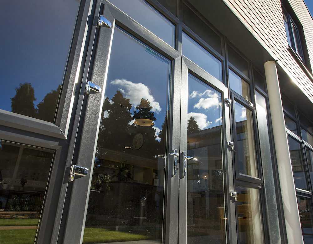 Close-up of gray French doors reflecting blue sky and clouds.
