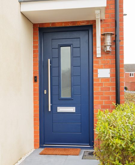 Modern blue composite door with a vertical glass panel, framed by red brick walls