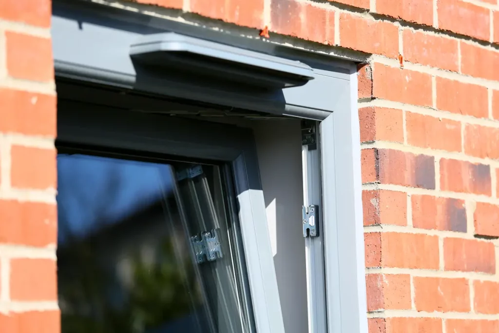 Close-up of a grey Liniar 70mm tilt and turn window installed in a brick property, showcasing the locking system and secure ventilation.